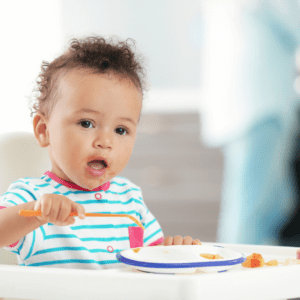 Main image for the article [4 Reasons Why It's OK To Combine Purees & Babyled Weaning!]. Pictured is a baby eating in their highchair. 