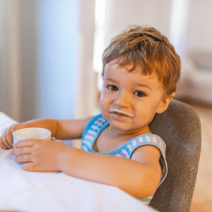 Main image for the article [How to choose the best type of milk for your baby & toddler]. Pictured is a toddler drinking milk from an open cup.