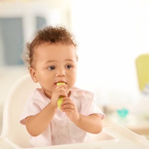 baby sitting in upright position in a high chair at the dinner table