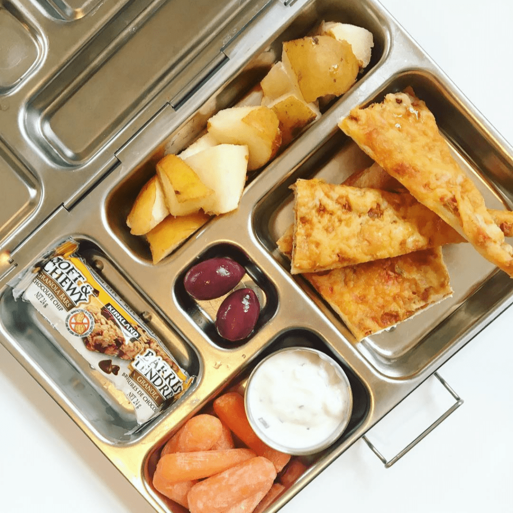 Main image for the article [How a simple mindset shift can remove the stress from lunch packing]. Pictured is lunchbox with pizza, carrots and dip, lives, pears and a granola bar.