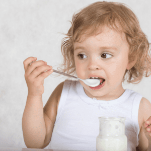 Main image for the article [Does My Child Need A Probiotic?]. Pictured is a toddler eating yogurt with a spoon. 