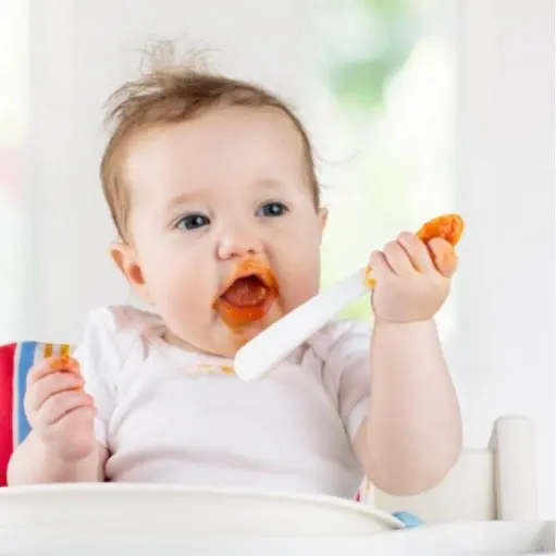 baby about six months old eating mashed sweet potatoes