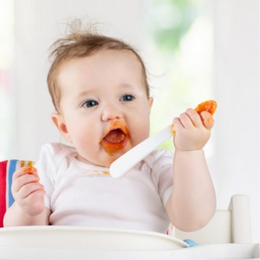 baby about six months old eating mashed sweet potatoes