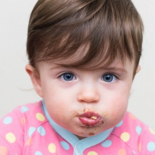 Pictured is a baby holding food in mouth. Example of stuffing mouth with food, food stuffing, pocket food