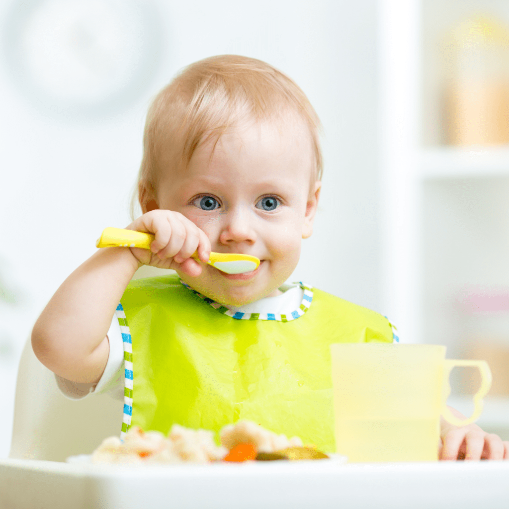 Main image for the article [How to Help Your Toddler Sit (and Stay) at the table]. Pictured is a toddler eating a plate of food in their highchair.