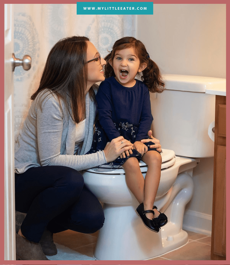 a mom squats down beside her daughter who is sitting on a toilet with a big smile on her face