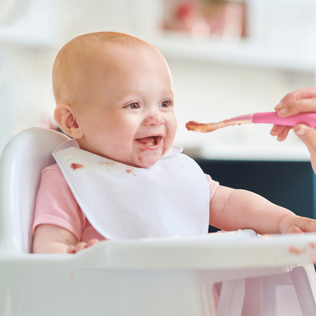Episode art for "#45: Understanding the readiness signs for starting solids: Purees & baby led weaning." Pictured is a baby in a high chair being spoon fed purees.