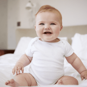 Featured image for article "Is Your Baby Ready for Solid Food?". Pictured is a baby sitting up on a bed.