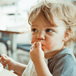 Featured image for article: "5 Tips for getting your picky toddler to try meat." Pictured is a toddler putting food into their mouth.