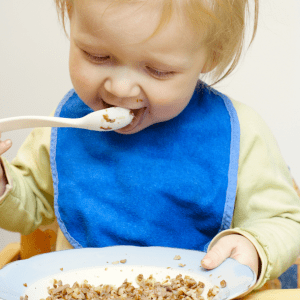Featured image for article: "The truth about serving grains and other starches to your baby". Pictured is a baby eating a bowl of oatmeal.