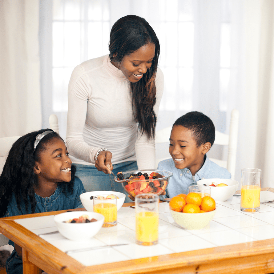 Featured image for article: "Proven phrases for getting your toddler to eat - without pressure or bribes!". Pictured is a mom serving her two children fruit.