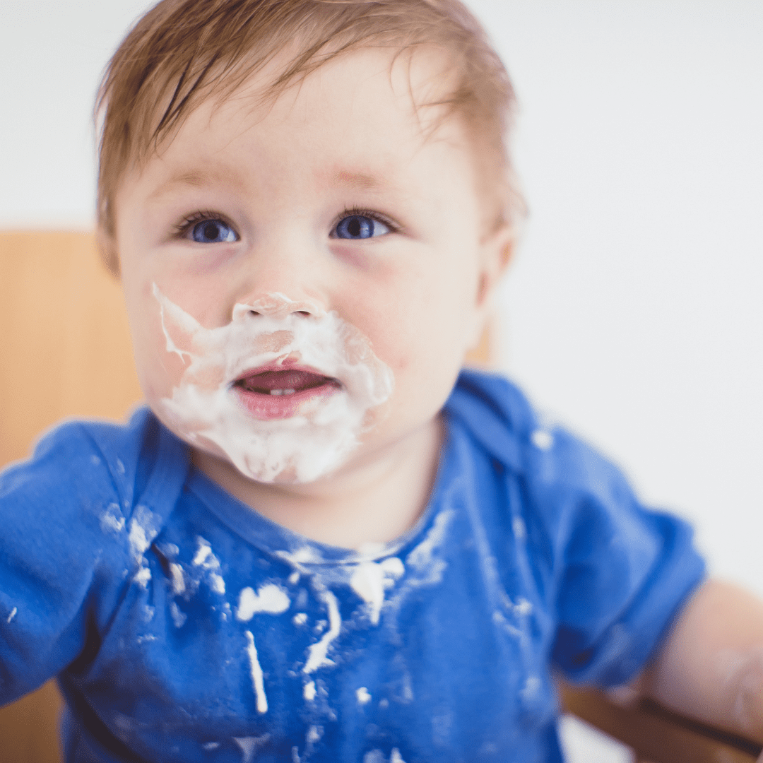 A baby with yogurt on their face from self-feeding by doing baby led weaning combined with purees.