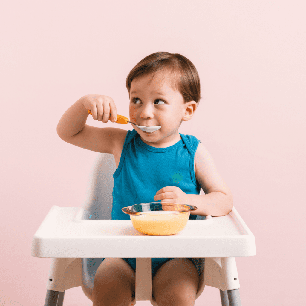 baby sitting in a high chair self-feeding with a spoon