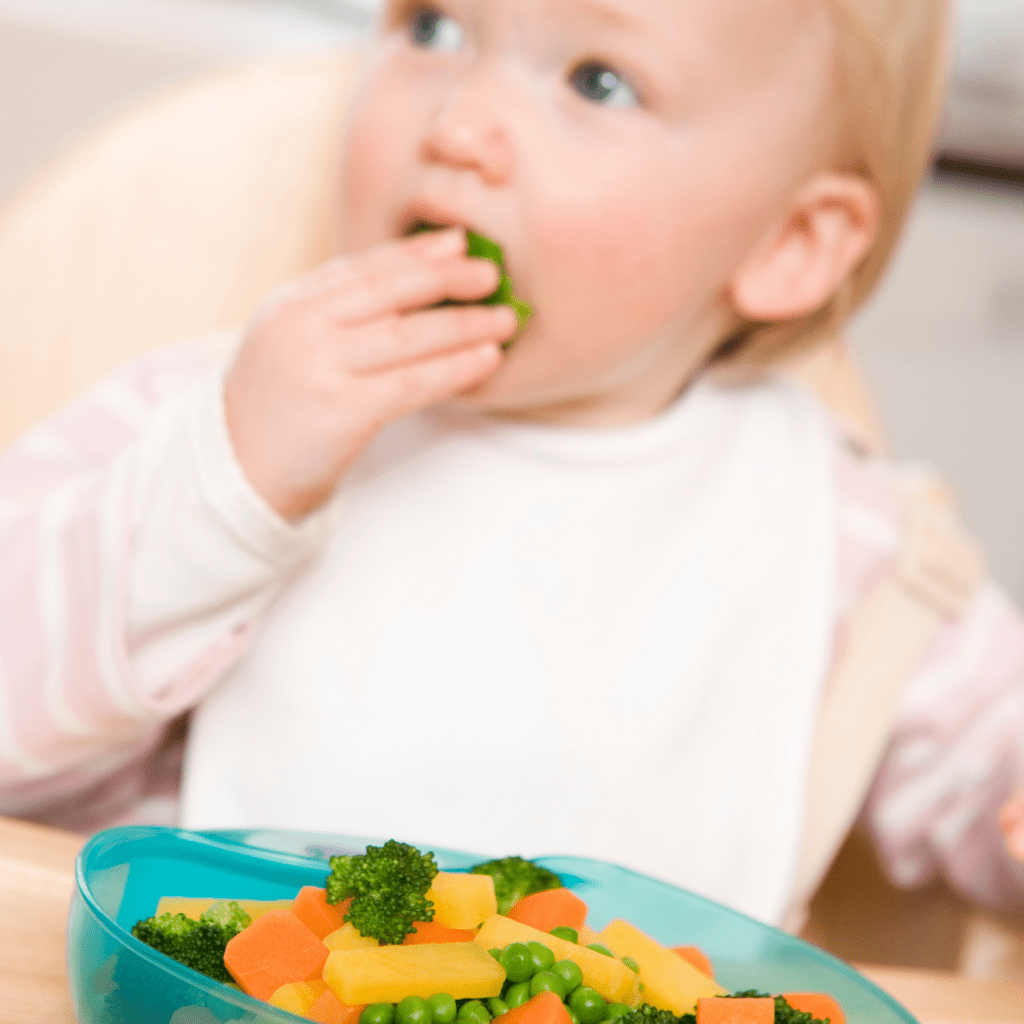 baby self-feeding on mixed veggies such as steamed broccoli