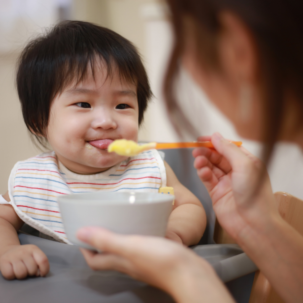 baby being offered pureed food, has tongue forward out of mouth