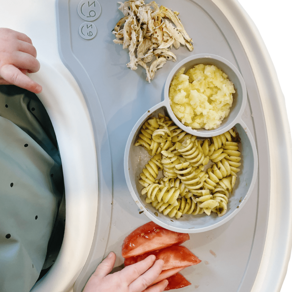 healthy lunch ideas for daycare; baby grabbing food from plate including shredded chicken and pesto pasta salad