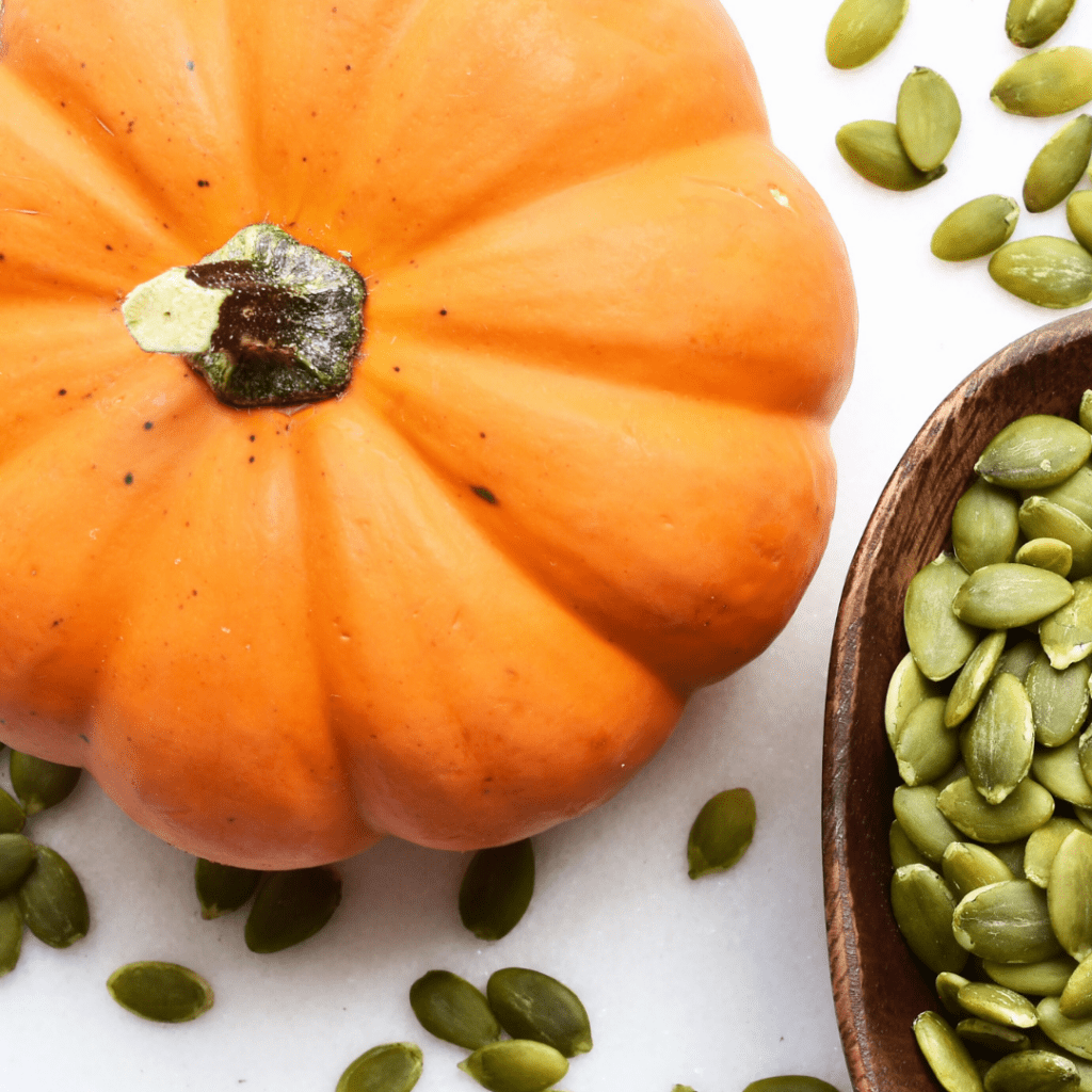Best pumpkin baby food; pictured is a fresh pumpkin and many pumpkin seeds in a bowl.