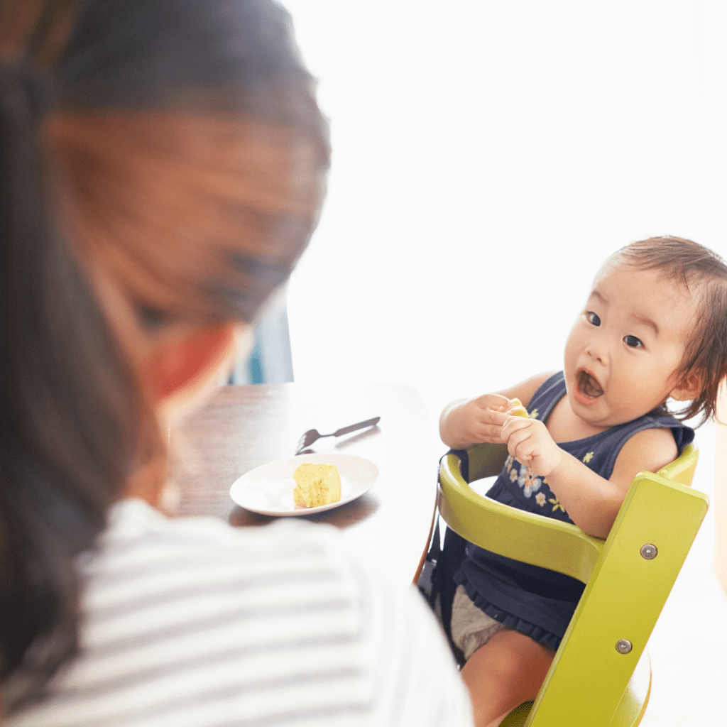 Baby eating cake in a high chair.