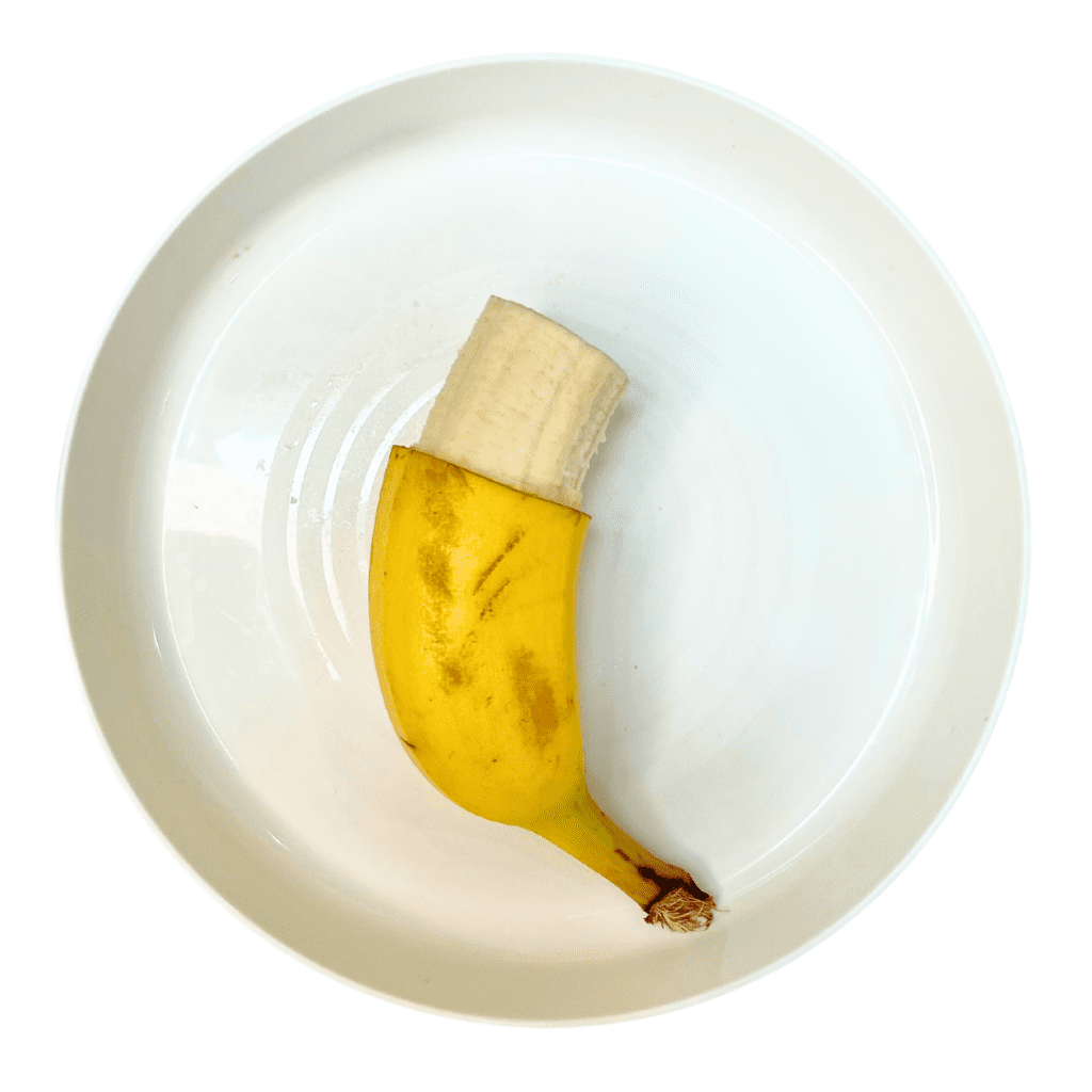 Banana pop on a plate; a banana with part of the skin on for grip when starting baby led weaning at 6 months.