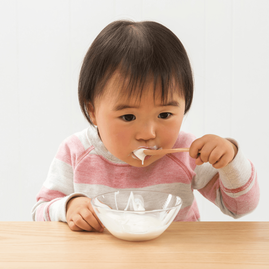 Starting solid foods by introducing top allergens as soon as possible to rule out food allergies early. Baby eating yogurt with a spoon, baby led weaning style.