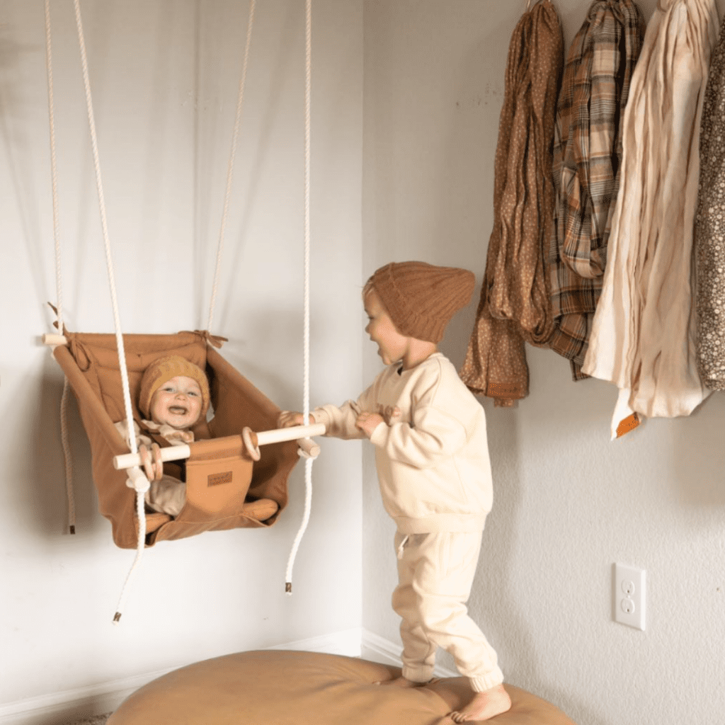 Toddler pushing baby in an indoor swing by Sweet Swinging.