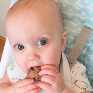 Baby eating a burger made from ground beef.