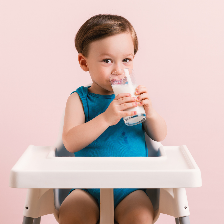 Toddler drinking milk in their high chair.