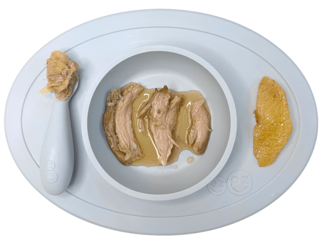 Baby plate containing moist, slow-cooked lamb with sauce and cooked apple wedge.