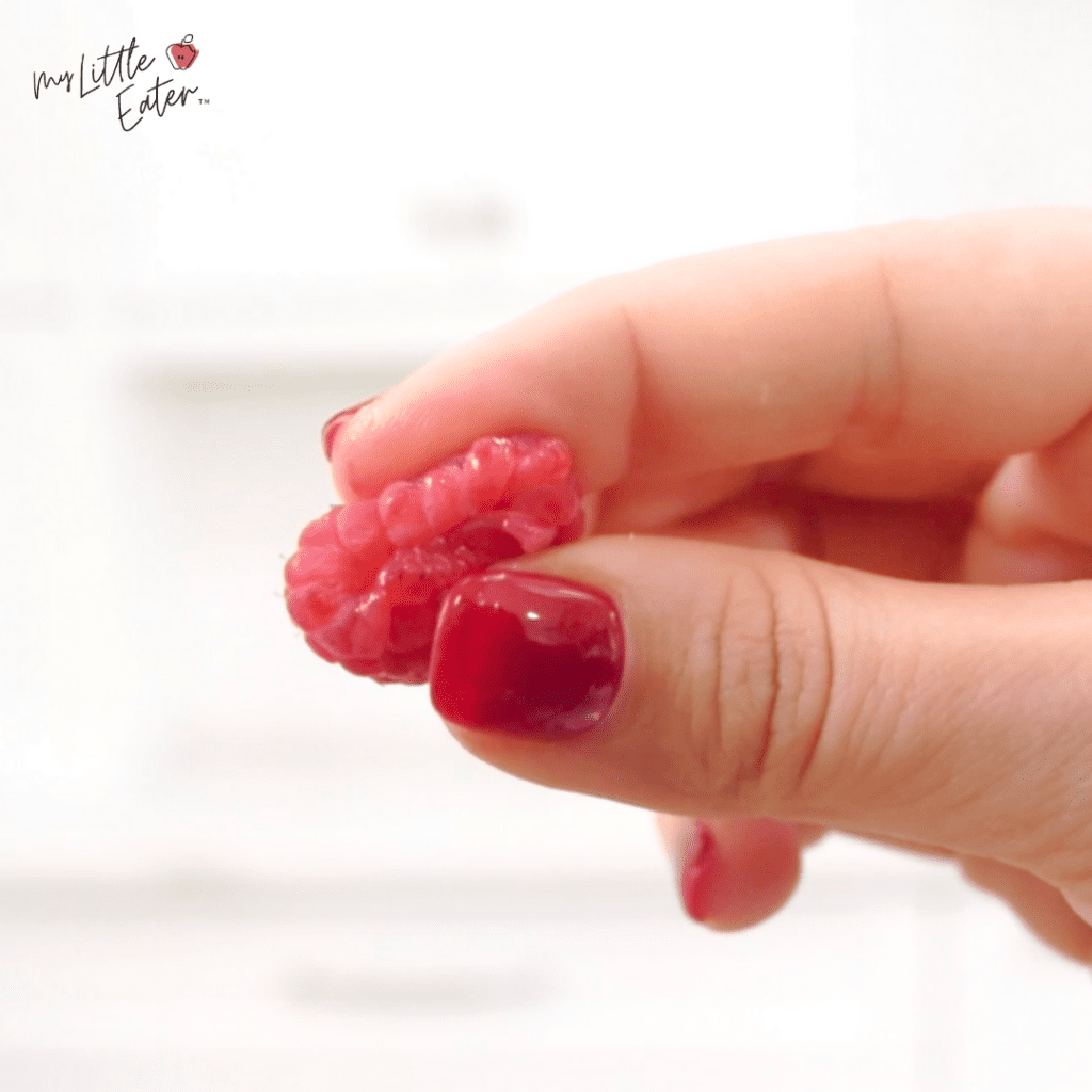Close-up of thumb and index finger performing the squish test on a raspberry.