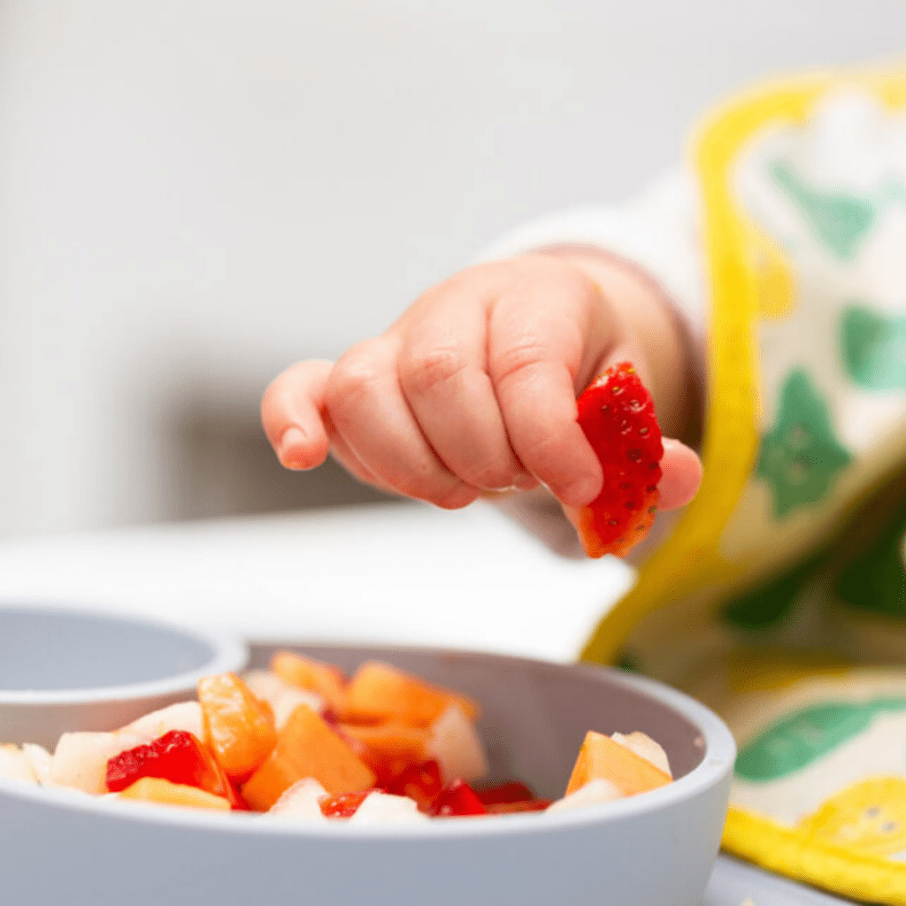 Close-up image of baby picking up a piece of strawberry with their pincer grasp for baby led weaning.