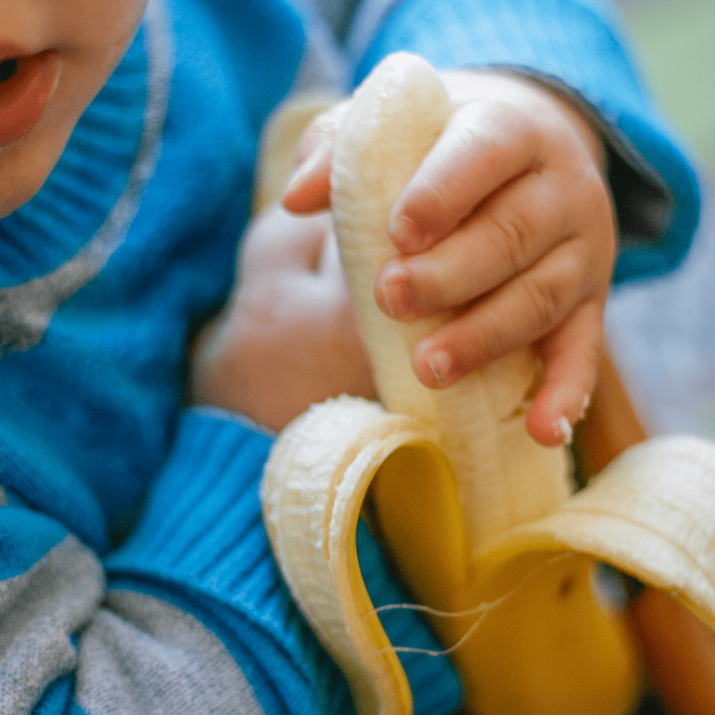 Close-up of a baby's hand grabbing a peeled banana with palmar grasp for baby led weaning.