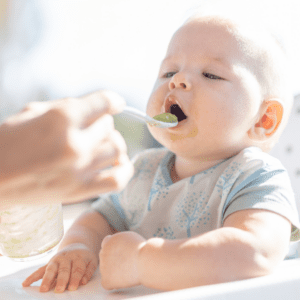 Baby being spoon fed pureed food in their high chair.