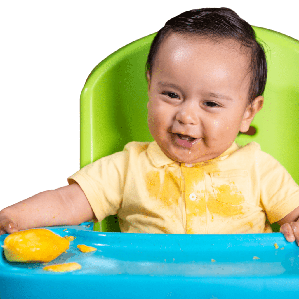 Baby in their high chair eating a mango pit as a finger food option.