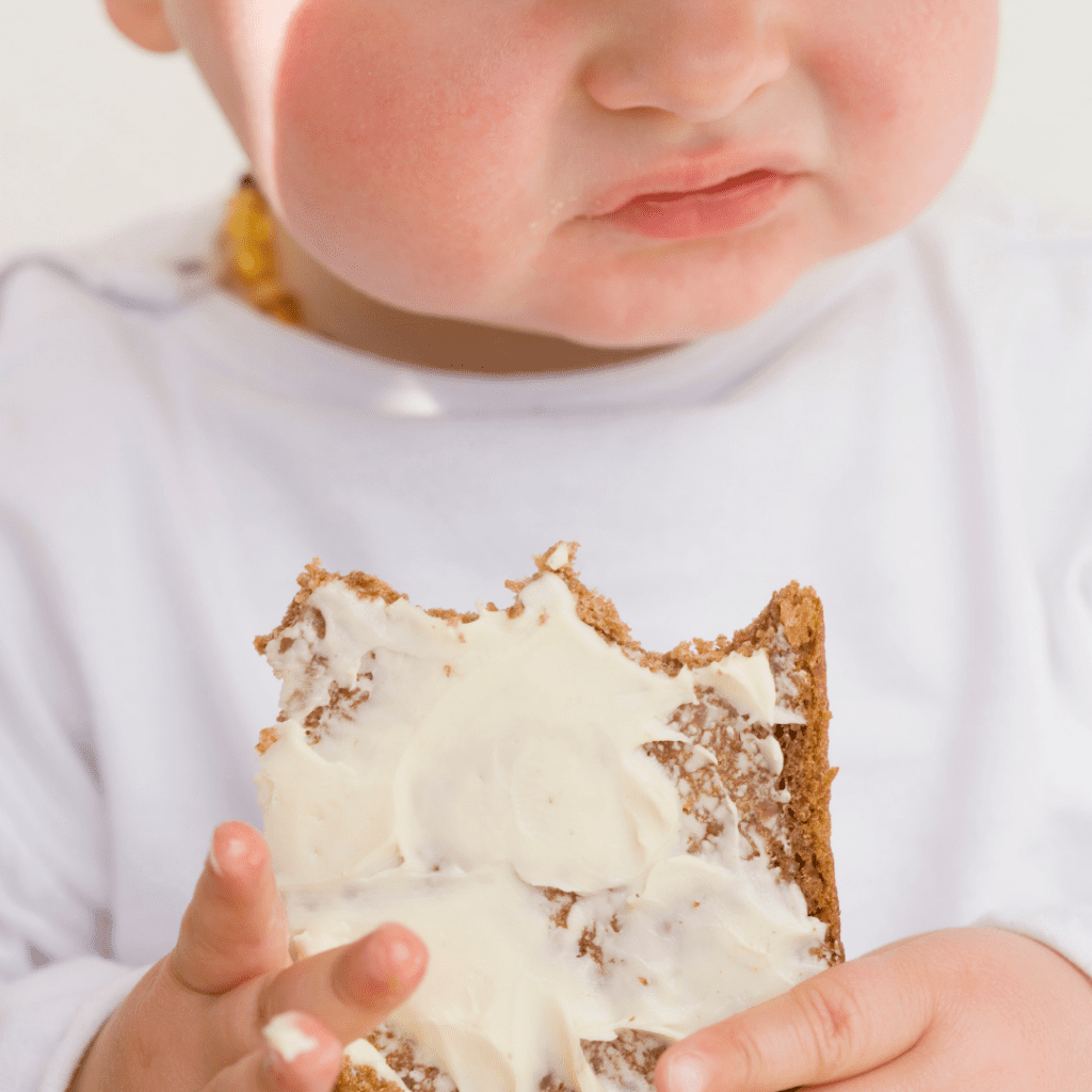 Baby eating toast with cream cheese.