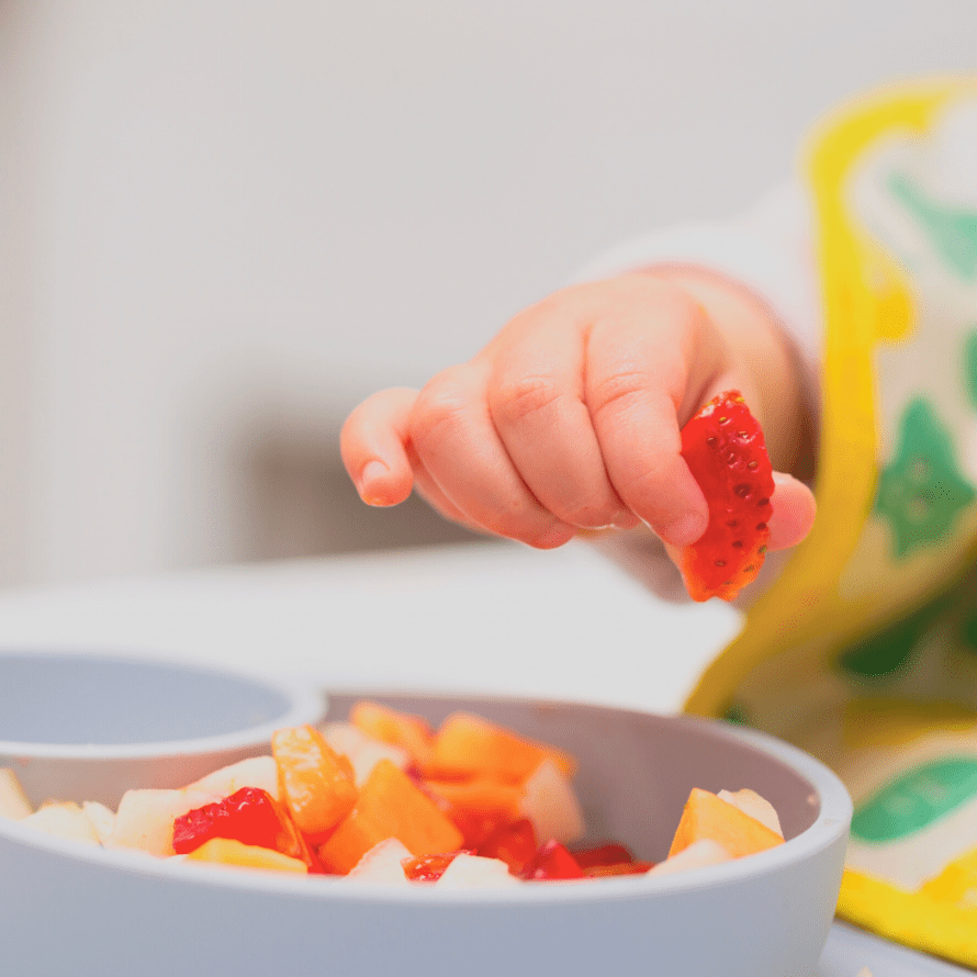 Baby eats various fruits cut up and served in a bowl.