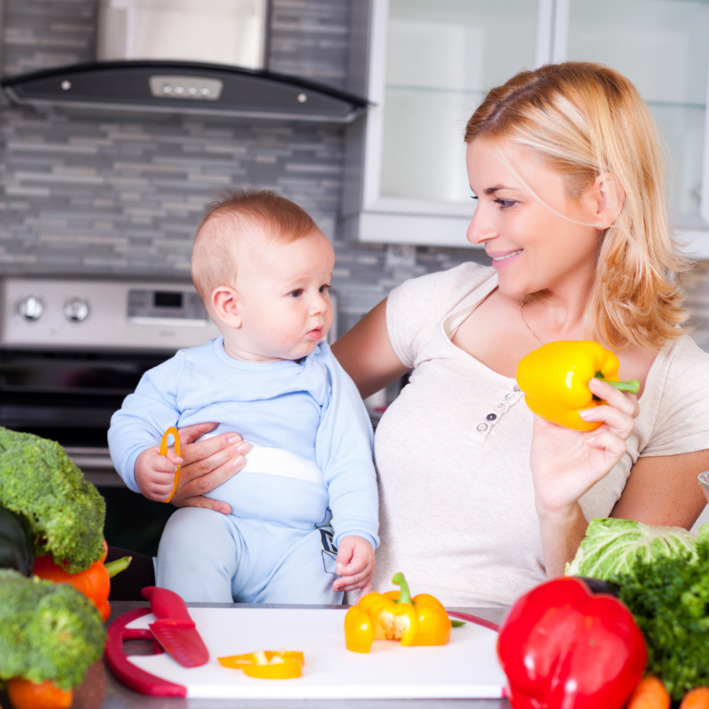 A baby watches their mom cut peppers; cooking with kids can begin as early as 6 months old.