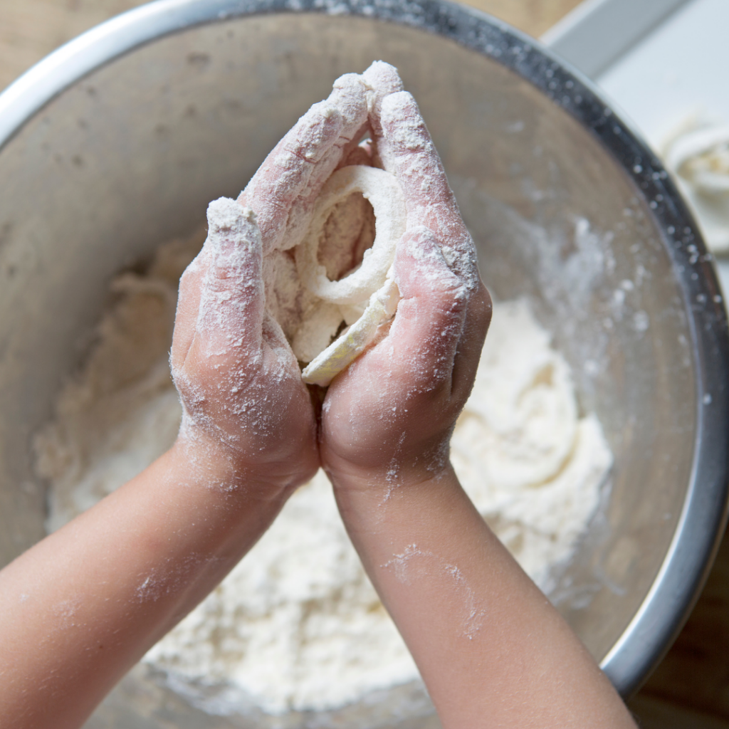 Messy toddler hands holding dough while cooking.