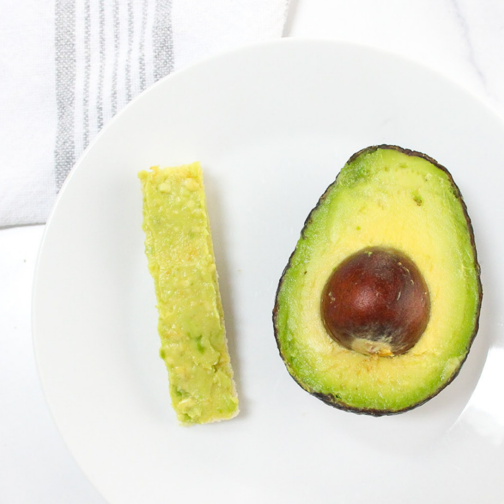 Half of an avocado plated beside a strip of avocado toast.