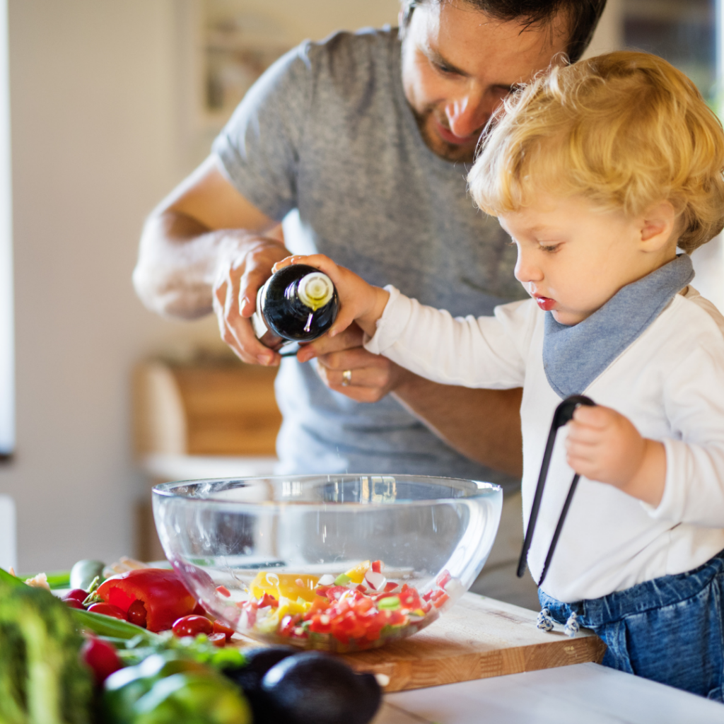 A toddler helps parent pour dressing on the salad.