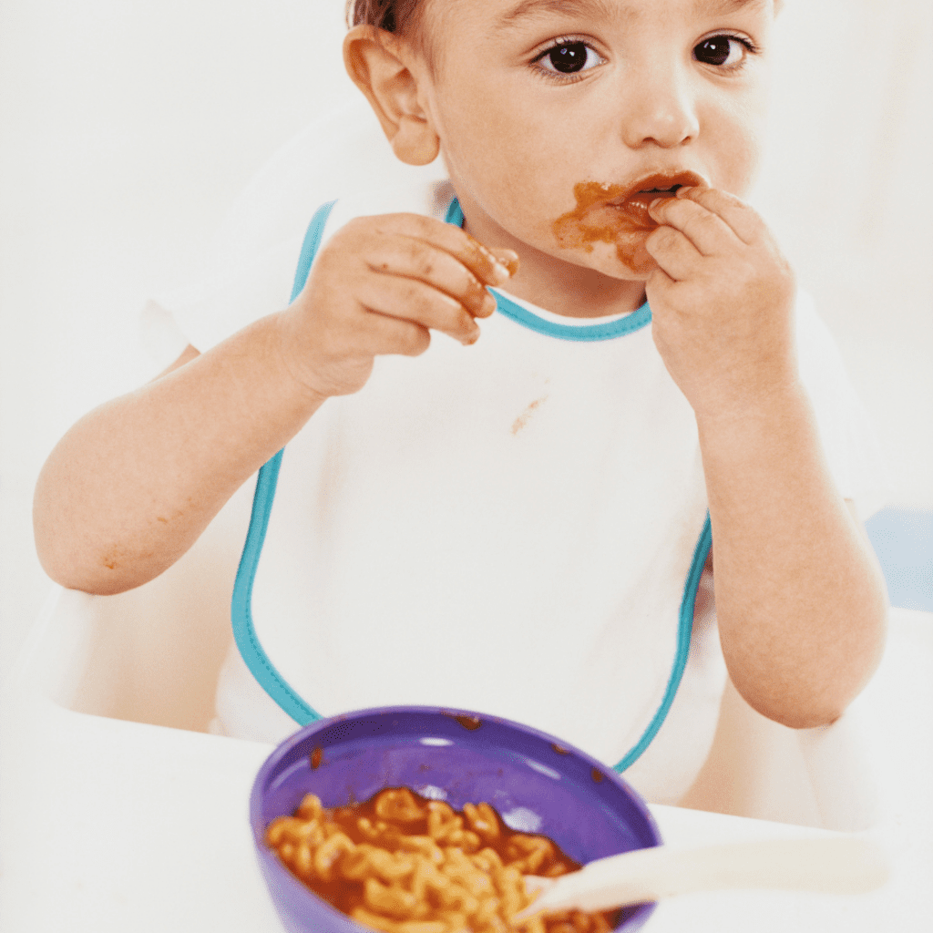 Baby eating cooked pasta, using their pincer grasp to bring it to their mouth.
