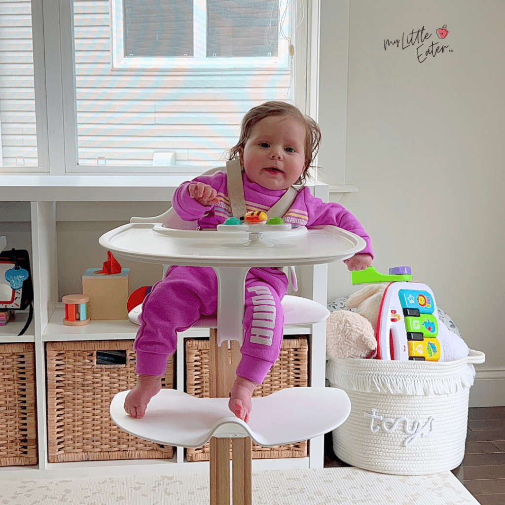 Baby at 5.5 months old in a high chair with toys, not ready to introduce solid foods because not sitting unassisted.