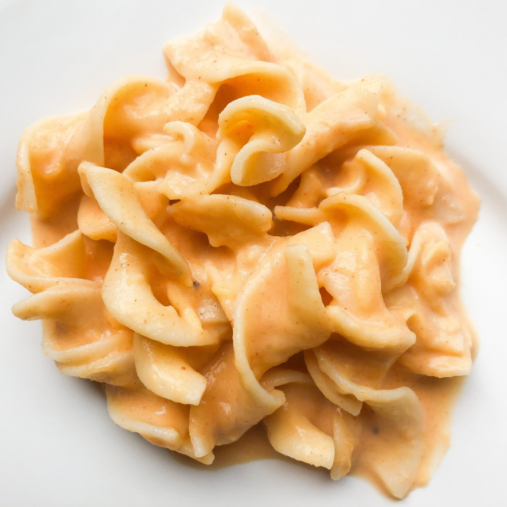 Pasta with a creamy sauce on a plate; serve pasta with sauce to help baby eat it safely.