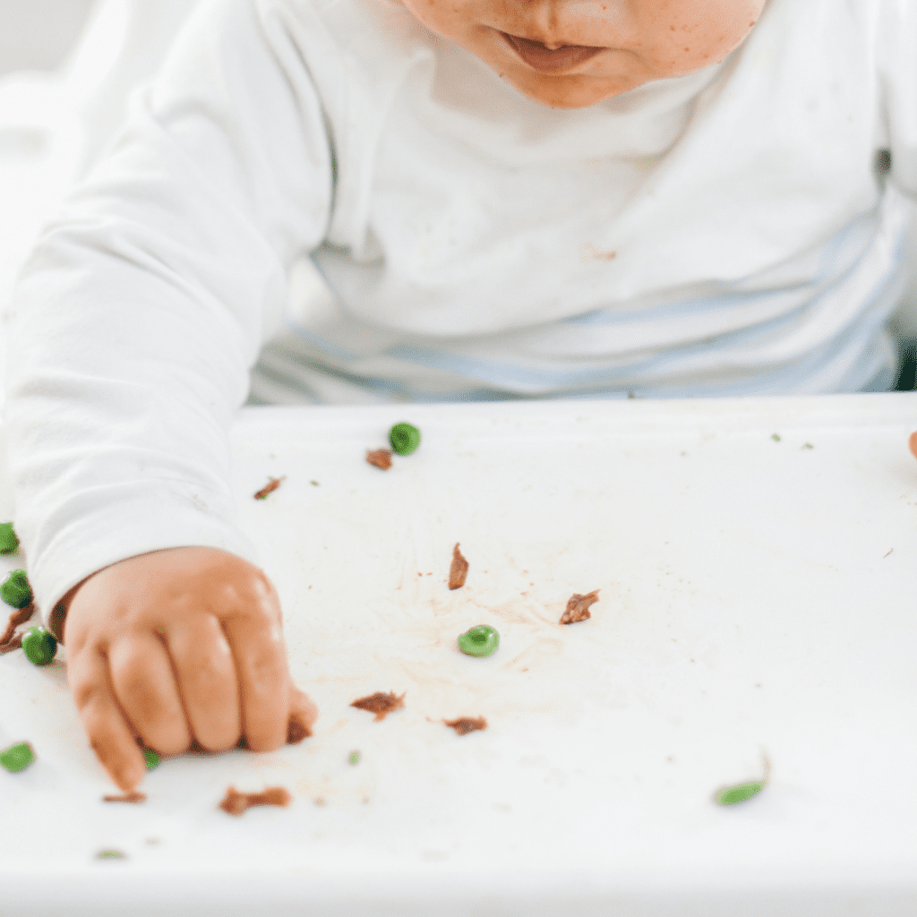 Baby picking up small pieces of shredded meat using their pincer grasp.