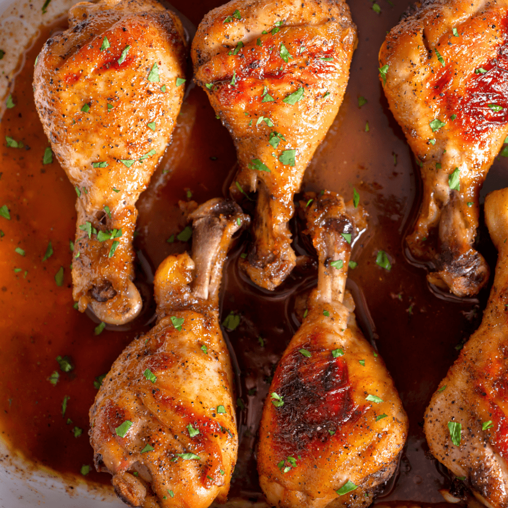 Cooked chicken drumsticks with the skin on and juice at the bottom of the baking dish.