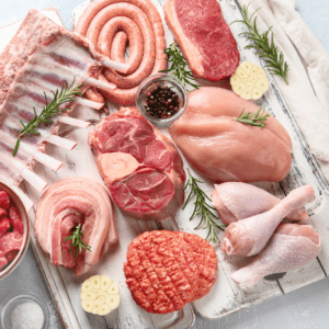 Different cuts of raw meat on a light background, surrounded by herbs and spices.