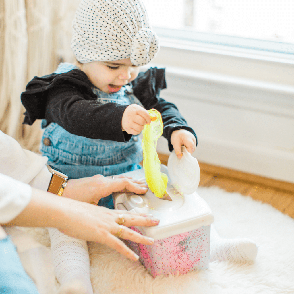 Baby sitting on the floor pulling colorful fabric out of a wipes container, one of the easiest pincer grasp activities to help baby learn.