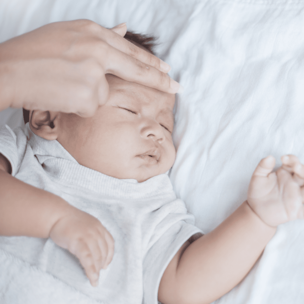 Parent checks temperature of their sick baby by feeling their forehead.