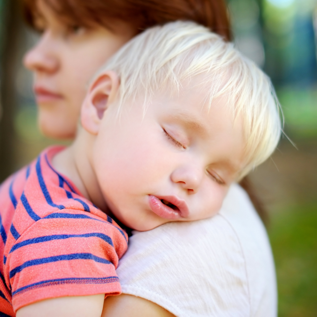 Sick child sleeps on their mother's shoulder.