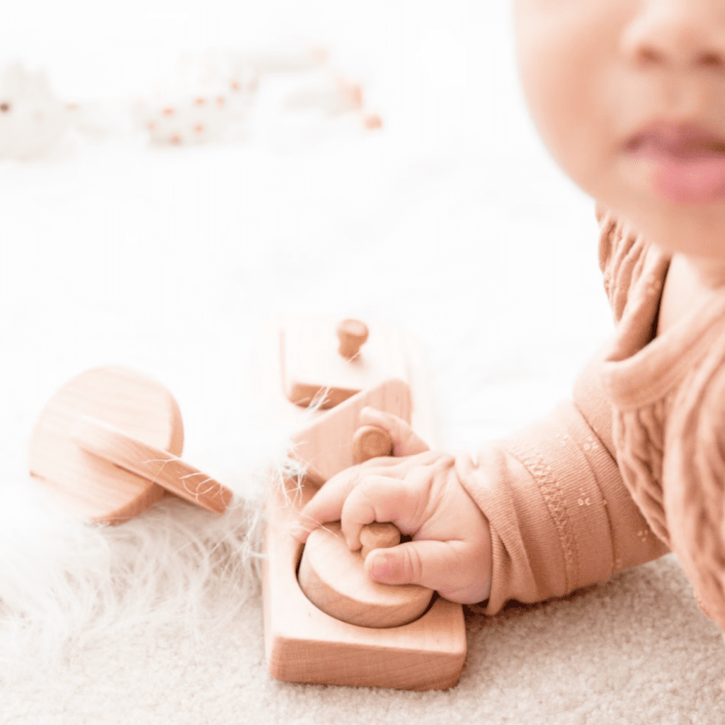Baby doing tummy time and playing with a wooden toy with a knob for baby's development.