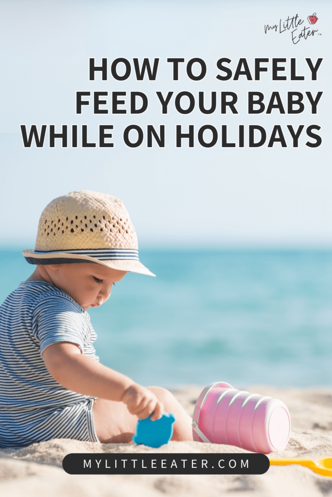 How to safely feed your baby while on holidays; baby boy sitting on the beach with a straw hat playing with beach toys.